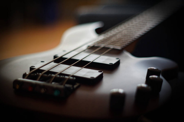 Close-up shot van een glad lichaam, pick-ups, brug, knoppen en snaren van een basgitaar muziekinstrument met achtergrondverlichting - Foto, afbeelding