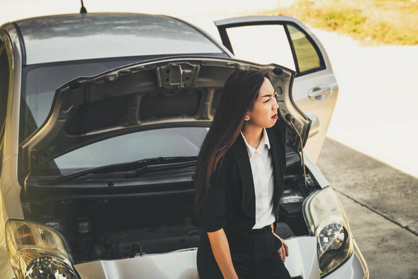 Азиатская деловая женщина открыла капот автомобиля, стоя перед машиной в отчаянии. Вызвав пустую трату времени на путешествия, она ждала помощи - Фото, изображение
