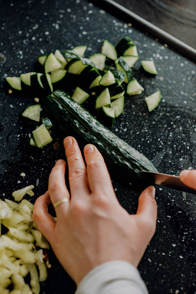 A vertical shot of hands cutting cucumber on the black surface - Photo, Image