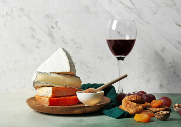 Ποτήρι κρασιού, διαφορετικοί τύποι τυριών και σνακ σε ελαφρύ φόντο - Φωτογραφία, εικόνα