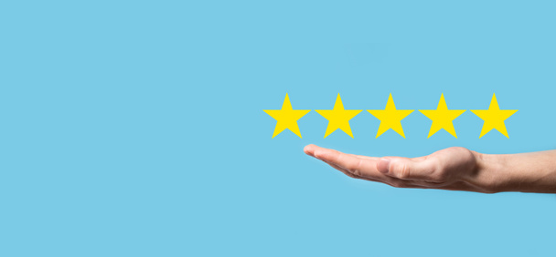 Человек держит смартфон в руках и дает положительную оценку, значок пятизвездочный, чтобы повысить рейтинг концепции компании на синем фоне. - Фото, изображение