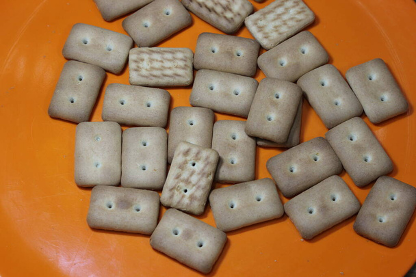 Vista superior cercana de galletas de galleta. Muchas galletas rectangulares con pequeños poros en plato rojo - Foto, imagen