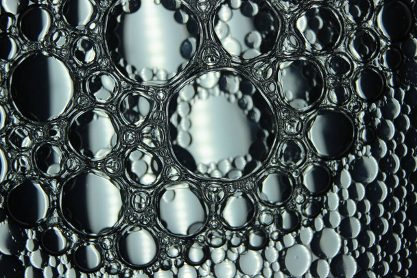 αφηρημένο υπόβαθρο μακροεντολή των κύκλων πετρελαίου που επιπλέουν πάνω από την επιφάνεια του νερού. Μακροσκοπική κοντινή άποψη των φυσαλίδων στο νερό. φυσαλίδες λαδιού στο μακροφωτογραφικό φόντο νερού - Φωτογραφία, εικόνα