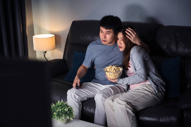 young scared couple is watching horror movie TV on sofa at night - Foto, Imagem
