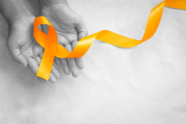 Hands holding orange color ribbon on white fabric with copy space. Kidney Cancer Awareness, Leukemia disease, Skin cancer awareness, World Cancer Day. Healthcare or hospital and insurance concept. - Photo, Image
