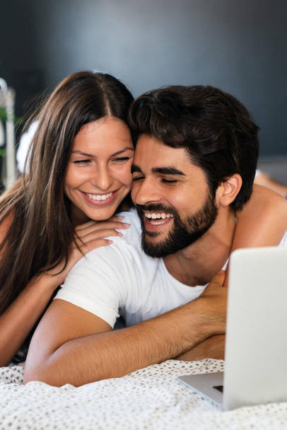 Young happy couple lying on bed at home and using laptop. - Photo, image