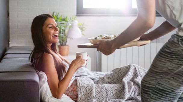 Happy man bringing the breakfast to his beautiful girlfriend on the bed - Foto, afbeelding