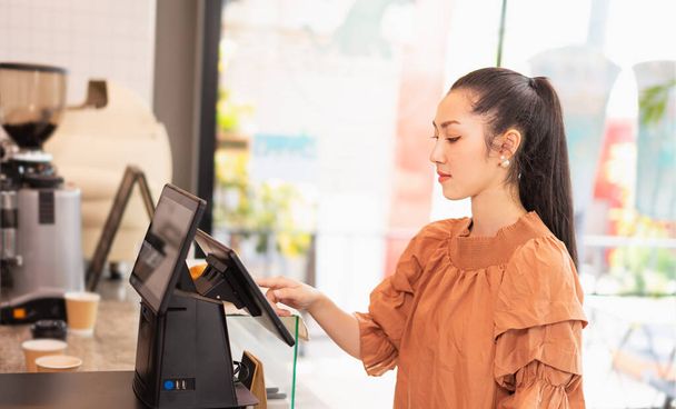 美しいアジアの女性の顧客の左側のコーヒーバーでレジ画面上のコーヒーの種類を選択します。コーヒーバーとフードサービスビジネスでバリスタの仕事 - 写真・画像