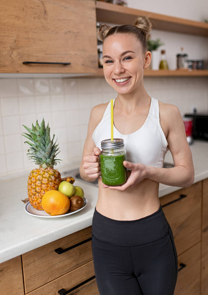 Cheerful woman with green detox drink at home - Fotoğraf, Görsel