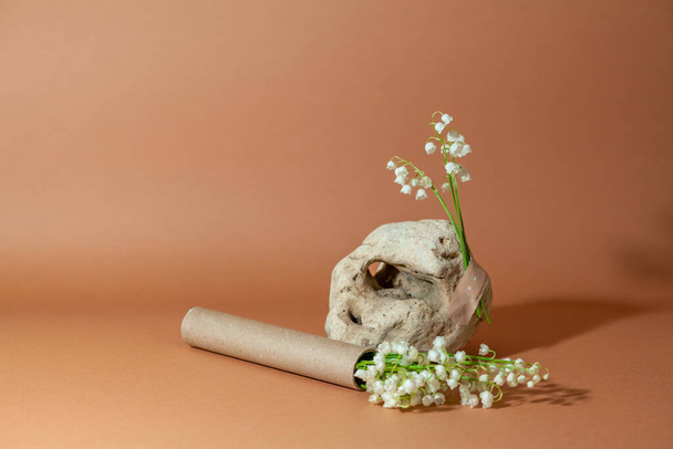 Modernes Stillleben mit ungewöhnlichem Naturstein mit Maiglöckchenstrauß und Pappröhrchen. - Foto, Bild