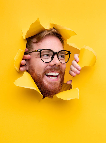 Happy man looking through torn paper hole - Foto, Imagen