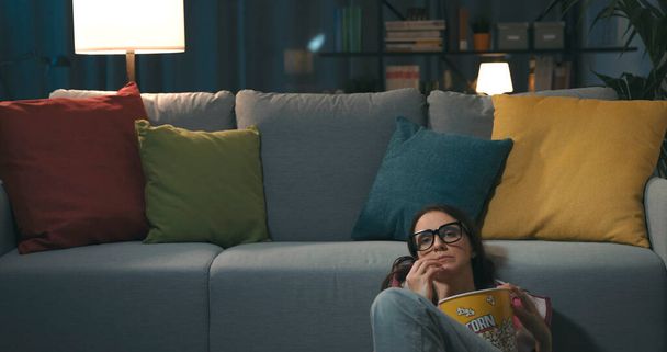 Žena doma kouká na televizi, sedí na podlaze a jí popcorn - Fotografie, Obrázek