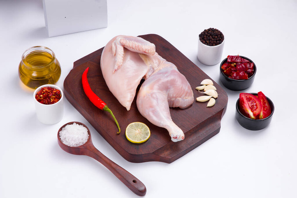 Rauwe halve kip zonder schil op houten plank versierd met kokende ingrediënten met een leveringsdoos op getextureerde stenen of grafiet achtergrond - Foto, afbeelding