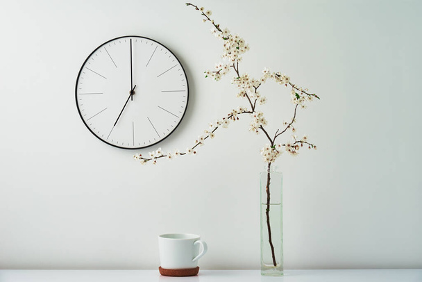 Wall clock, blooming branch and cup on white background - Photo, Image