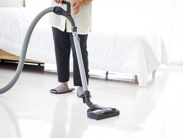 Aziatisch senior oudere vrouw huisvrouw stofzuigen de vloer op slaapkamer met stofzuiger, oma doet huishoudelijk werk in huis. - Foto, afbeelding