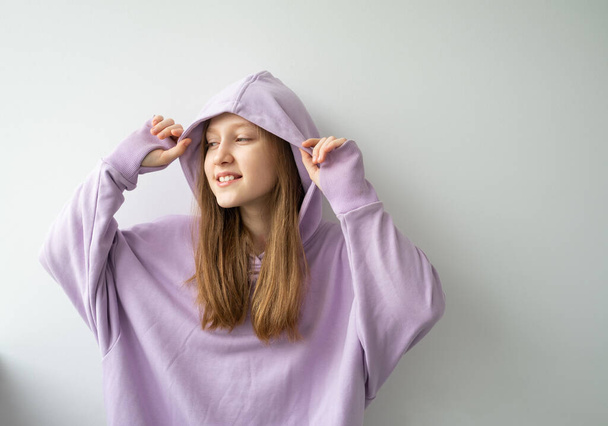portrait of beautiful teenage girl with long hair in purple hoodie standing against white wall. - Photo, Image