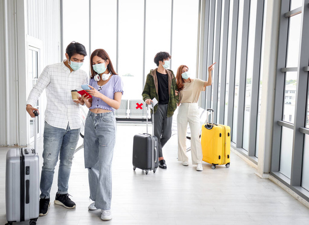 Aziatische jonge toeristische groep met bagage dragen gezichtsmasker om coronavirus infectie te voorkomen, staan op de luchthaven, wachten luchtvaartmaatschappij vlucht op terminal, sociale afstand en nieuwe normale reis concept. - Foto, afbeelding