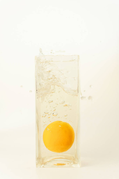 A vertical shot of a glass of splashing water with a small orange isolated on a beige background - 写真・画像