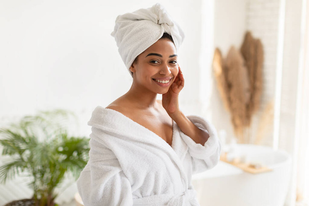 魅力的なアフリカ系アメリカ人女性が浴室に立って頬に触れる - 写真・画像