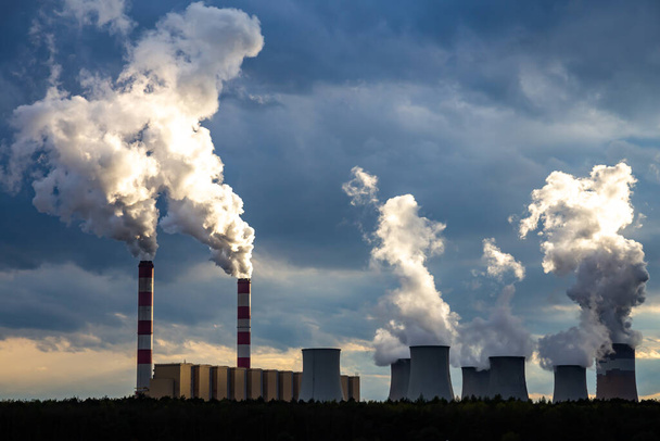 Ein Blick auf die rauchenden Schornsteine eines Kohlekraftwerks vor dem Hintergrund eines dramatischen Himmels mit Wolken. Das Foto wurde bei Tageslicht aufgenommen. - Foto, Bild