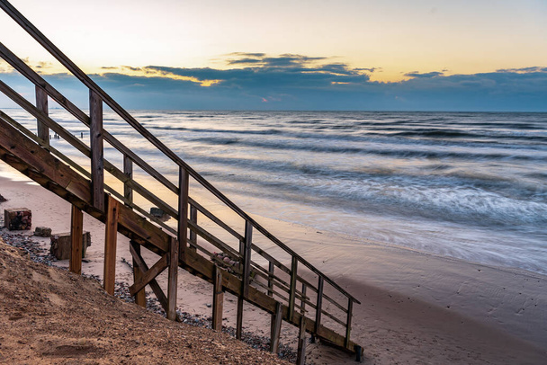 μια ξύλινη σκάλα που σας επιτρέπει να φτάσετε στην ακτή της παραλίας πολύ κοντά στην ακτογραμμή του νερού, ακριβώς όπως για να πάει απευθείας στο νερό της θάλασσας - Φωτογραφία, εικόνα