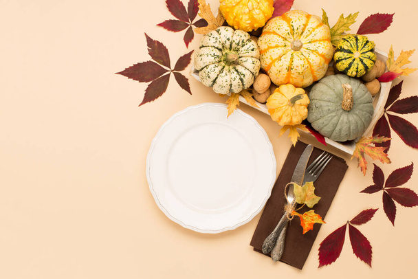 Autumn fall holiday Thanksgiving table place setting. Pumpkins, porcelain white plate, dry maple leaves, spice and apple on beige pastel background. Flat lay, top view, copy space. - Photo, Image