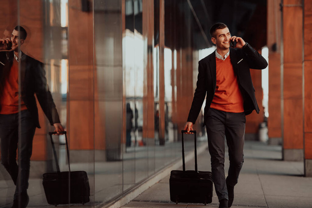Going to airport terminal. Confident businessman traveler walking on city streets and pulling his suitcase drinking coffee and speaking on smartphone - Fotoğraf, Görsel