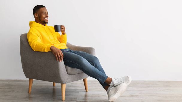 Αφρικανός τύπος πίνοντας καφέ κάθεται στην καρέκλα πάνω από γκρι φόντο - Φωτογραφία, εικόνα