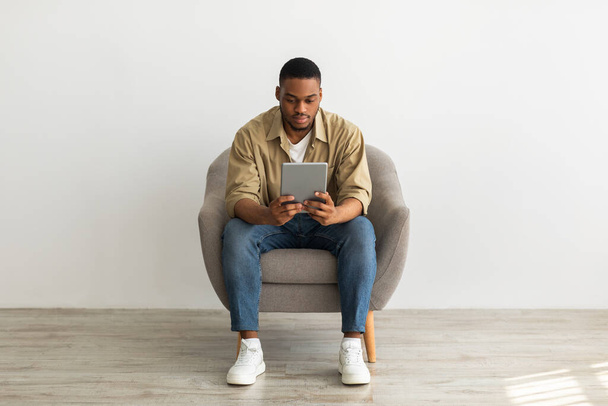 Zwarte man met behulp van digitale tablet zitten over grijze muur achtergrond - Foto, afbeelding