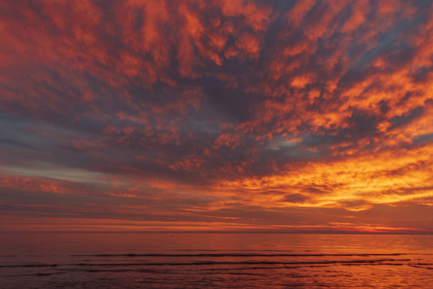 okamžik po západu slunce, kdy slunce zmizelo za obzorem a zbarvilo mraky a vodní hladinu v zajímavých červenooranžových odstínech - Fotografie, Obrázek