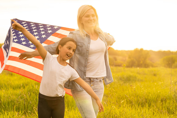 Patriotic holiday. Happy family, mother and her daughter child girl with American flag outdoors. USA celebrate 4th of July - Photo, Image