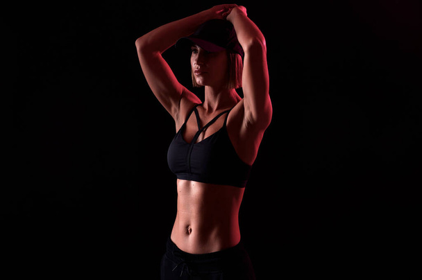 Starke Frau in Sport-BH mit muskulösem Bauch vor schwarzem Hintergrund. Perfekte Körperform - Foto, Bild