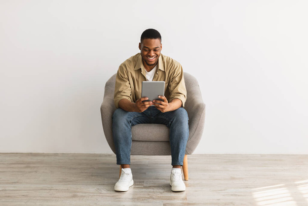 Happy African Man Korzystanie z tabletu cyfrowego siedzi na szarym tle - Zdjęcie, obraz