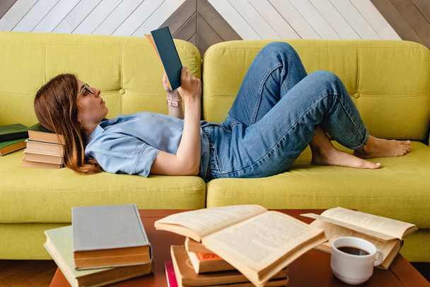 Νεαρή γυναίκα που διαβάζει στον καναπέ στο σαλόνι - Φωτογραφία, εικόνα