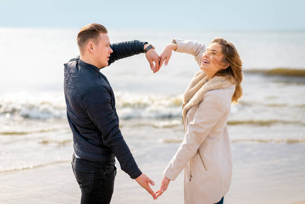 若い夫婦が春や秋の夜に海のビーチで腕を組んでハートの形を作っている. - 写真・画像