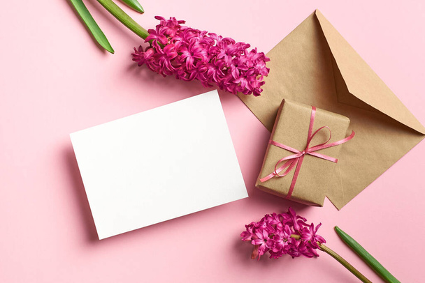 Greeting or invitation card stationary mockup with envelope, gift box and fresh hyacinth flowers on pink background, top view, copy space - 写真・画像