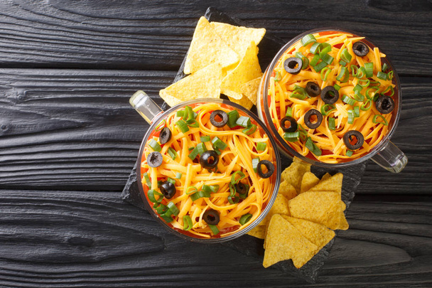 Classic Mexican 7 Layer Dip with corn chips close up in the glass on the table. Horizontal top view from abov - Photo, Image