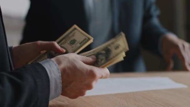 Nahaufnahme bis zur Unkenntlichkeit kaukasischer Geschäftsmann sitzt Geld am Tisch und gibt Bündel von Dollars Gehaltszahlung an unbekannte afrikanisch-amerikanische Spezialanwältin Agent, Anlagekonzept - Filmmaterial, Video