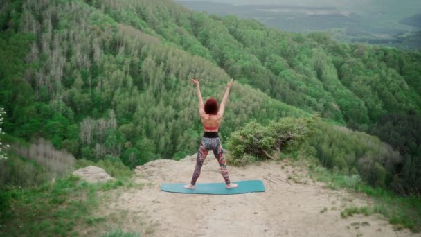 Athletic woman practices yoga on top mountain. Slim girl goes in sports outdoors - Footage, Video
