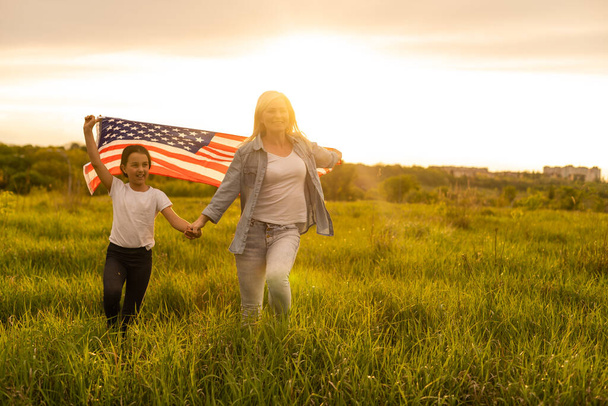 美しいフィールドにアメリカ国旗を持つ母と娘 - 写真・画像
