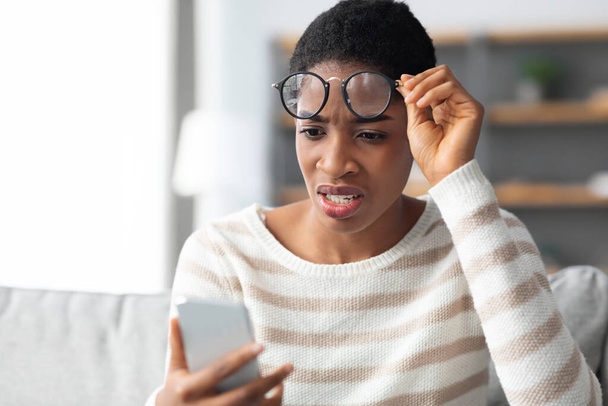 Malo mensaje. Mujer africana conmocionada quitándose las gafas y mirando la pantalla del teléfono inteligente - Foto, imagen