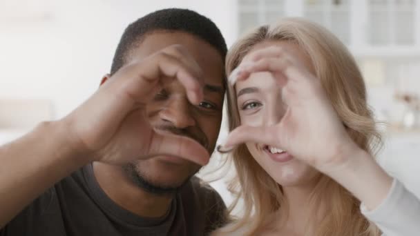 Diversa pareja mostrando el gesto del corazón sonriendo a la cámara en interiores - Metraje, vídeo