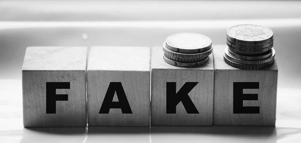 FAKE слово написано в дерев'яних блоках і стосах монет. Концепція бізнесу та новин
. - Фото, зображення