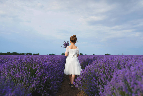 girl walking away with bouquet in lavender field - Fotó, kép