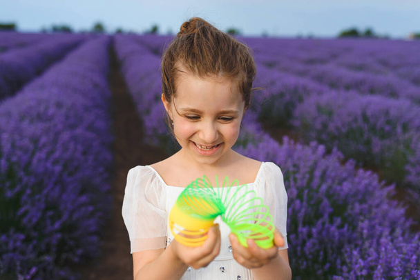 smějící se dívka drží slinky hračka v levandulovém poli - Fotografie, Obrázek