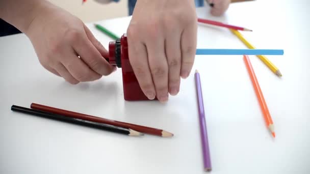 χέρι κρατά Μηχανική ξύστρα μολυβιών με χρωματιστά μολύβια σε λευκό φόντο. Πίσω στο σχολείο. προετοιμασία σχολικών χαρτικών για τη μελέτη - Πλάνα, βίντεο