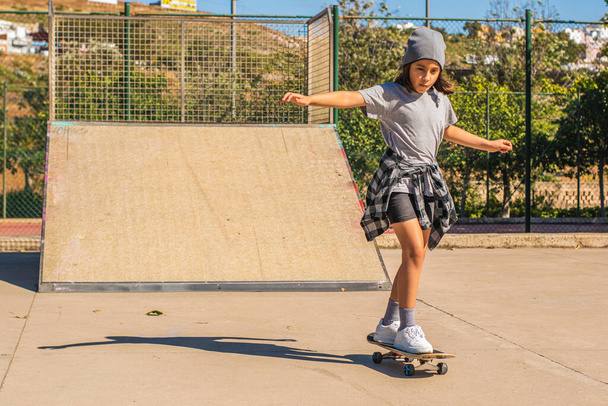 Caucasian girl dressed in footwear skating with her skateboard in a skate park - Foto, Imagem