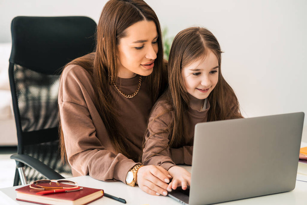 Mère et fille font leurs devoirs à l'ordinateur portable. Petite écolière à distance à la maison - Photo, image