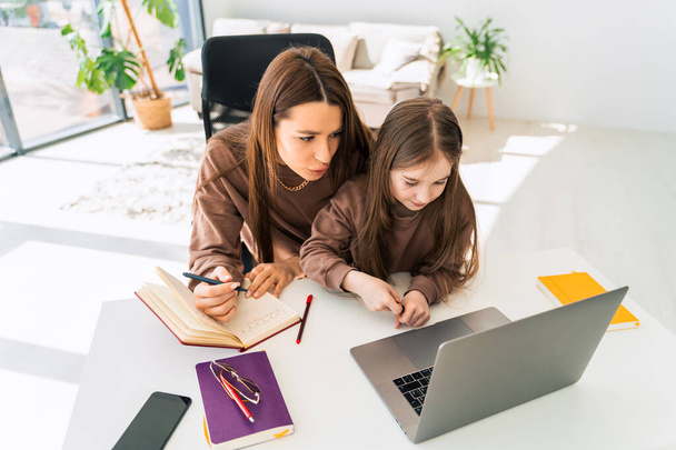 Anya és a kislánya házit csinálnak a laptopon. Anya otthon tanítja a gyereket. - Fotó, kép