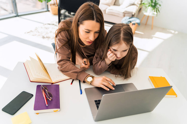 Maman et petite fille font leurs devoirs sur ordinateur portable. Mère enseigne à l'enfant à la maison - Photo, image